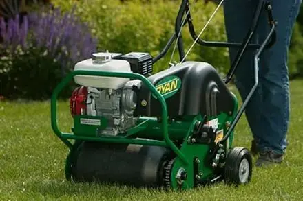 A person is using a green and black lawn mower on a lush green lawn.